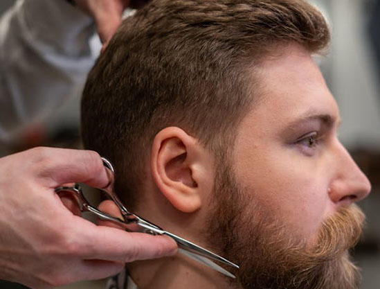 A hairdresser uses scissors to trim the side of a man's hairstyle, showcasing expert barbering techniques in a salon setting.