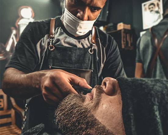 A barber delicately shaves a client's beard in a cozy barbershop atmosphere, surrounded by vintage decor and grooming tools.