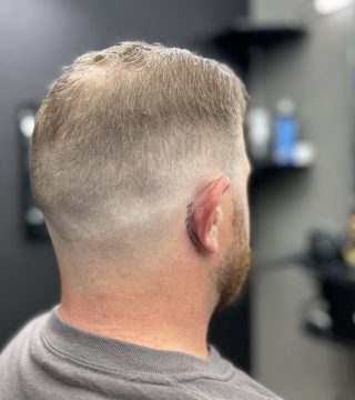 A man with a shaved head sits in a barber chair, ready for a haircut.