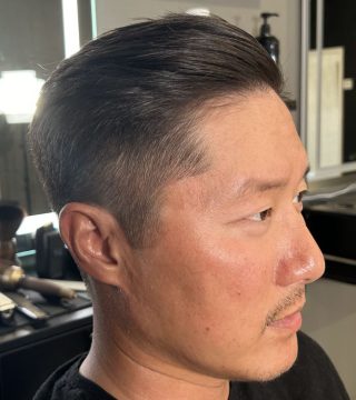 A man with a shaved head sits in a barber chair, ready for a haircut.