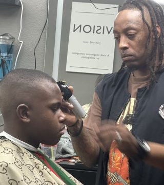 A man receiving a haircut from another man in a barbershop setting.