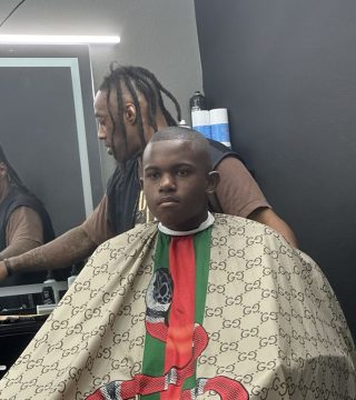 A young man receiving a haircut in a barber shop, seated in a chair with a barber working on his hair.