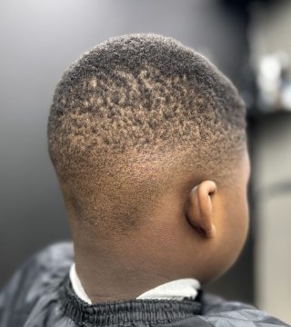 A young boy with a shaved head sits in a barber chair, looking content during his haircut.
