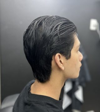 A man with black hair is getting a haircut in a modern salon setting.